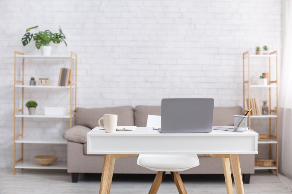 Remote Workplace Or Home Office During Coronavirus Outbreak. Sofa, Chair, Table With Laptop, Cup And Notepad In Living Room Interior